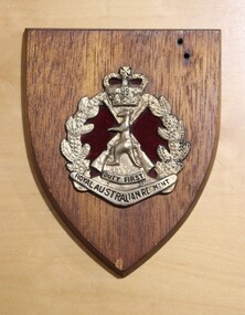 Wooden plaque with gold metal and red velvet decal, depicting insignia of RAR, Kangaroo, crossed rifles, crown, wattle wreath and boomerang.