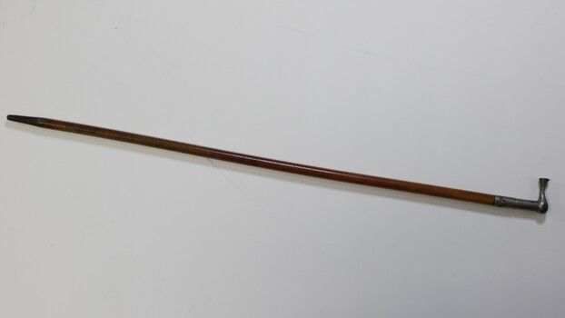 Wooden stick varnished with tarnished metal hilt with etched design that resembles mountains. Tip of stick is coloured black.