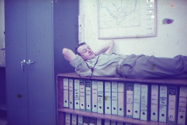 Dr Major Peter Byrne, laying on low bookcase containing arch lever folders.
