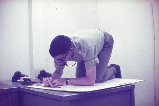Lt Steve Phillips kneeling on desk drawing on large paperwork.