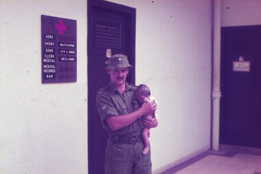 Soldier holding a baby on his hip.