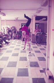 Female entertainer bending forward with male entertainer doing handstand on her back.