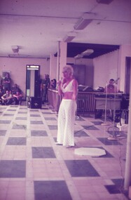 Female singer in white bikini top and white long pants.