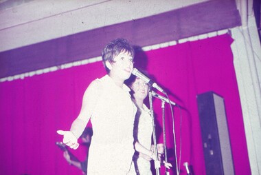 Two female entertainers in white dresses performing at microphones.