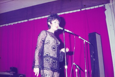 Female entertainer in black lace dress performing at microphone.