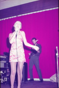 Female entertainer in pink shimmery dress performing with microphone in hand.