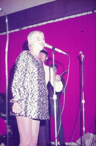 Female in gold shiny dress performing at microphone.