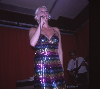 Female performer in striped sparkling outfit, microphone in hand.