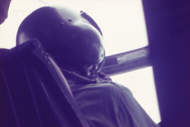Pilot wearing black helmet in cockpit of aircraft.
