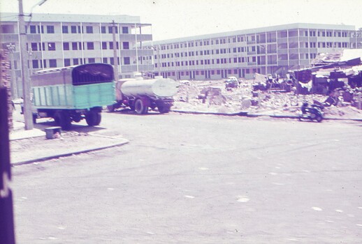Street with a truck and tanker parked beside rubble of buildings.