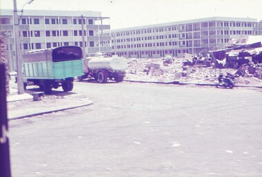 Street with a truck and tanker parked beside rubble of buildings.