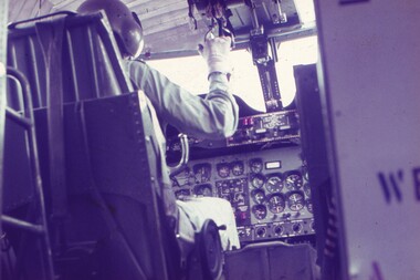 A pilot in the cockpit taken from behind, showing aircraft instruments.