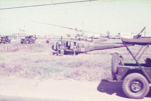 Medical helicopter landing in grass field, with medical trucks in background.