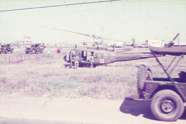 Medical helicopter landing in grass field, with medical trucks in background.
