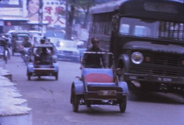 Motorised rickshaws traveling on a road with buses, bikes and vehicles.