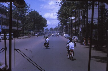 View of road taken from the windscreen of a bus of locals on bikes and vehicles ahead.