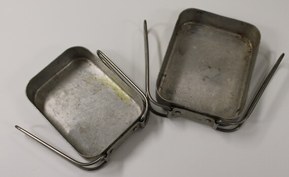 Two metal mess tins with folding handles. One fits inside the other.