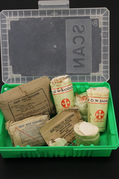 Small green plastic box with clear lid with bandages, electrolyte powder, safety pins. 