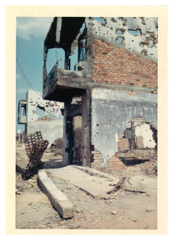 Coloured photo of a damaged building with holes and debris in the foreground.