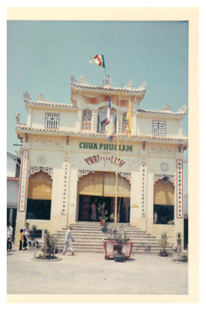 Buddhist pagoda. White ornate building with a flag pole flying the Vietnamese flag. 