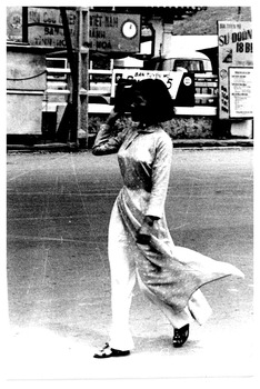 A sepia coloured photo of a woman walking along a street.