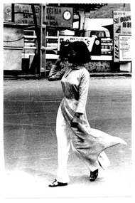 A sepia coloured photo of a woman walking along a street.