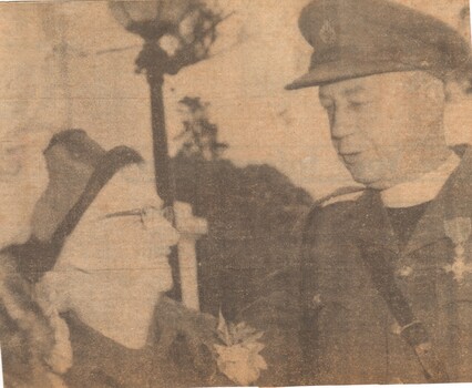 A Newspaper Clipping of Father Harry Brennan Talking To A Well Dressed Lady