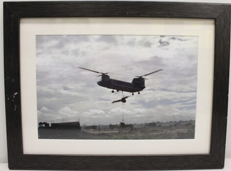 A Framed Coloured Photograph of a Boeing CH-47 Chinook Helicopter with a 105mm Howitzer Being Carried
