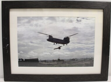 A Framed Coloured Photograph of a Boeing CH-47 Chinook Helicopter with a 105mm Howitzer Being Carried