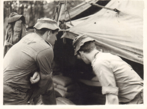 A Black and White Photograph of Two Soldiers Looking Into a Tent