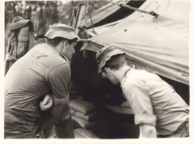 A Black and White Photograph of Two Soldiers Looking Into a Tent