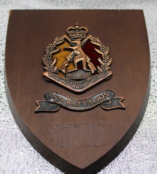 Small wooden plaque with metal badge afixed.