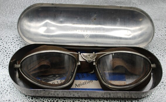 Small metal case containing aviators goggles and small booklet.