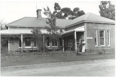 Polychrome brick cottage, L-fronted with bullnose verandah, on bluestone foundations with low bluestone fence. "Antiques" signs on building. 