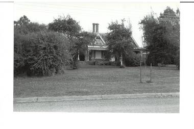 Photo of house partly obscured by trees, gable front over verandah, twin ornate chimneys