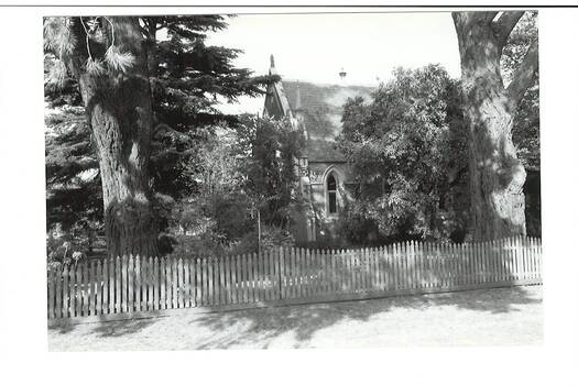 Side view of church building, part hidden  by trees, picket fence.