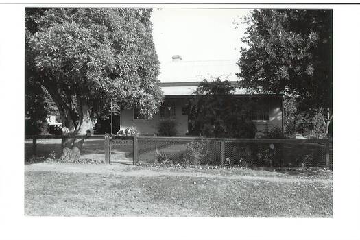 Weatherboard house, tin roof, verandah, framed by trees, wire fence.