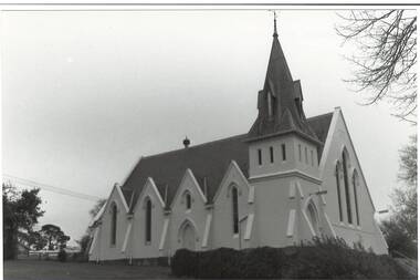 Uniting Church looking uphill from eastern side, white rendered, showing four gables and five buttresses, belltower and steeple, slate roof.  Formerly Presbyterian Church