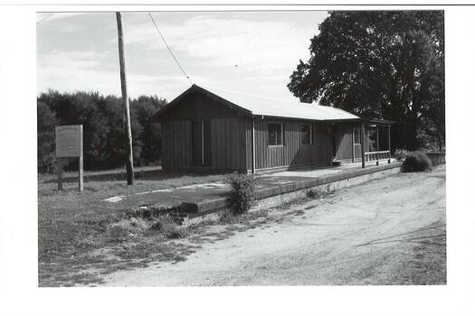Remains Buninyong Railway Station platform, (built 1889) sign on left, power pole and Tennis Club shed, elm tree behind right..