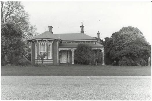 Victorian polychrome brick dwelling, bay window left, verandah right with iron lace, trees either side