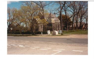 Colour photo, across street, bluestone church partly hiddden byy autumn trees, original brich school/hall visible behind.