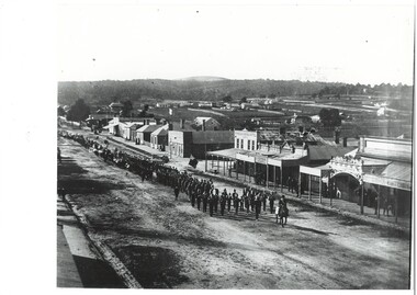Street view, from hotel balcony, procession led by man on horseback, then rass band and marchers, buildings along road, scattered houses and ridge beyond.