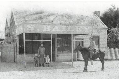 Weatherboard shop and dwelling, verandah, signage, picket fence Man in butcher's apron with two children,, man on horseback right foreground.