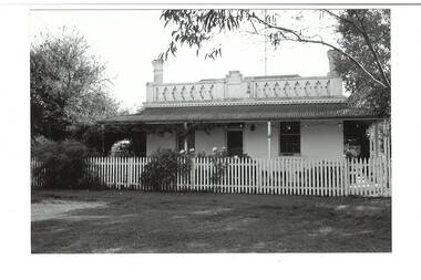 Single front white rendered cottage, ornate geometric parapet, bullnose verandah, two chimneys, picket fence
