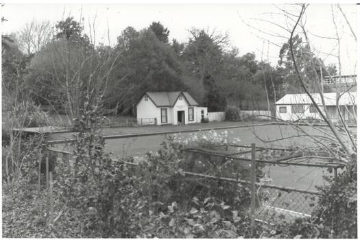 B/W photo Buninyong Bowling Club, over fence and garden and across Bowling Green, modern clubhouse on right, old 1870's Clubhouse Centre. 