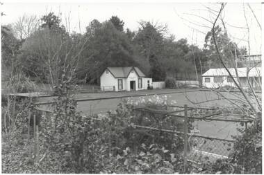 B/W photo Buninyong Bowling Club, over fence and garden and across Bowling Green, modern clubhouse on right, old 1870's Clubhouse Centre. 