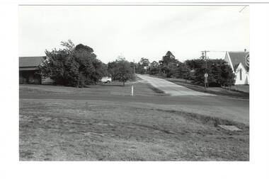 View across intersection, old house on left, church on right, car parked between trees.
