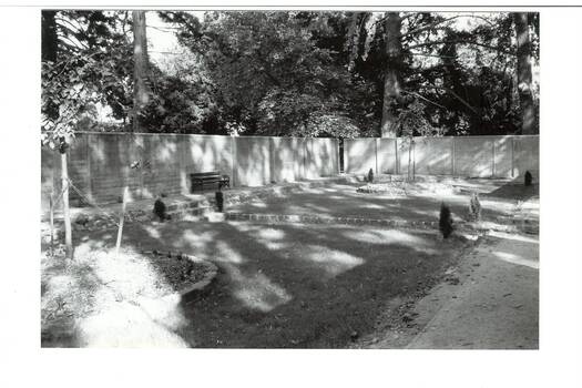 Concrete walls , side and back, tall trees behind, sunken lawn (not sown) bluestone surround