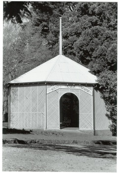 Octagonal rotunda, wooden lattice walls, iron roof, flagpole, arched entrance, trees surrounding