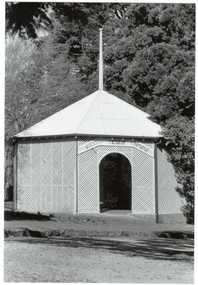 Octagonal rotunda, wooden lattice walls, iron roof, flagpole, arched entrance, trees surrounding